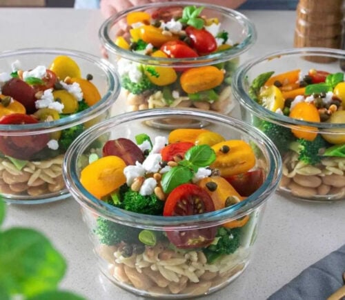 Photo shows four colorful bowls of orzo, bean, and pesto salad on a table