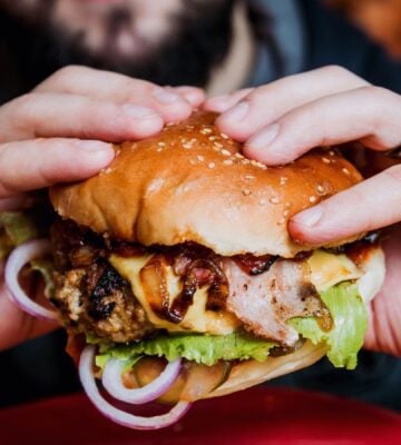 Photo shows a man's hands as he holds a meat-based burger up to the camera