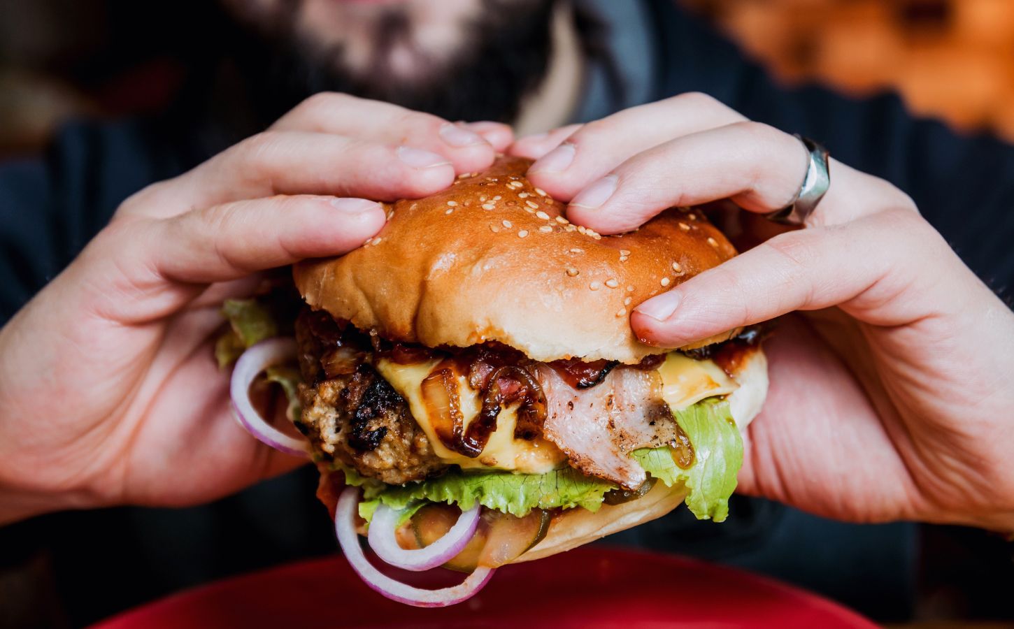 Photo shows a man's hands as he holds a meat-based burger up to the camera