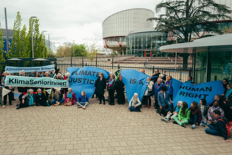 Photo shows the women of KlimaSeniorinnen celebrating their victory outside the ECHR with flags and banners