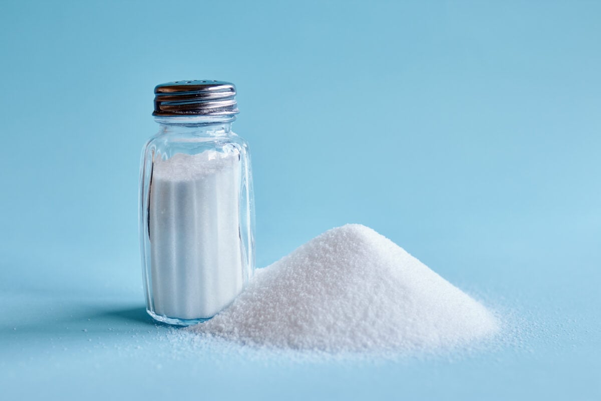 Photo shows a salt shaker next to a loose pile of salt on a pale blue background
