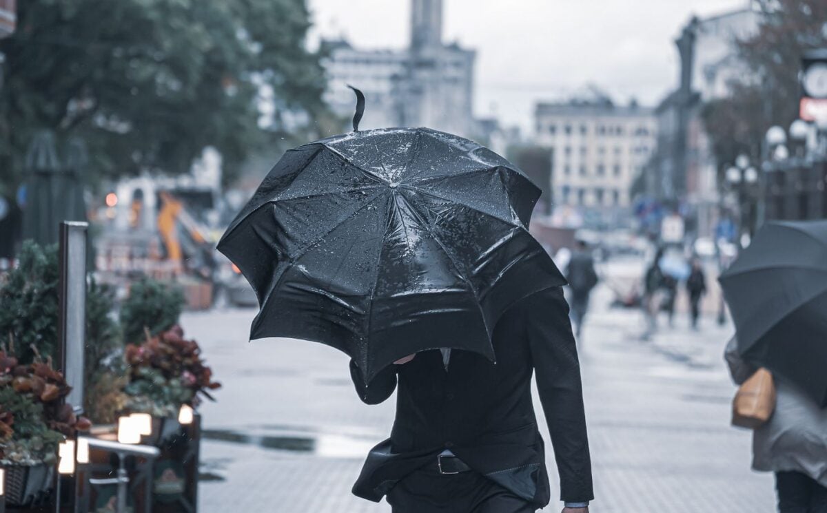 Photo shows someone in a suit walking with a black umbrella held low against heavy rain