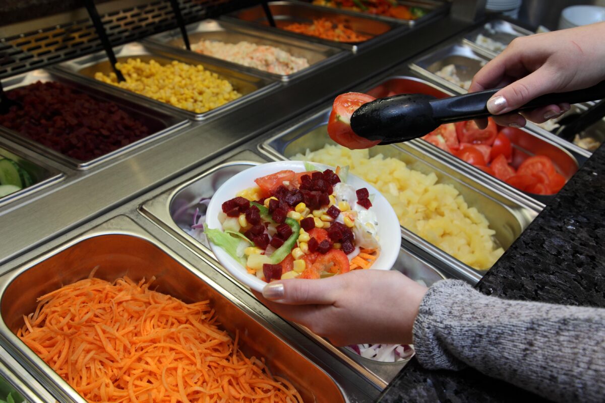 A person serving themself salad at a Harvester salad bar