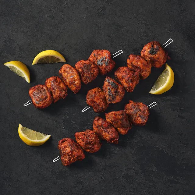 Photo shows the classic Shicken plant-based chicken Tikka Kebab product cooked and arranged on a slate with sliced lemon