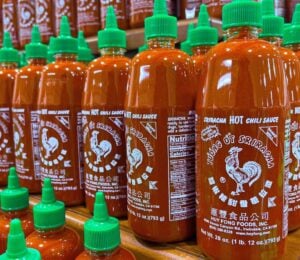 Photo shows several shelves stacked with Huy Fong Foods' Sriracha chili sauce in its distinctive bottles with green caps