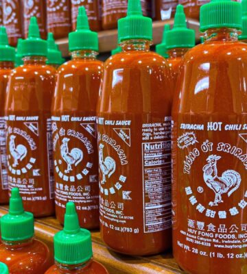Photo shows several shelves stacked with Huy Fong Foods' Sriracha chili sauce in its distinctive bottles with green caps