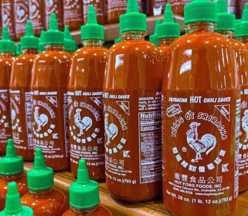 Photo shows several shelves stacked with Huy Fong Foods' Sriracha chili sauce in its distinctive bottles with green caps
