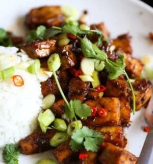 Photo shows a bowl of black pepper tofu garnished with scallions and served with white rice, prepared to a vegan recipe