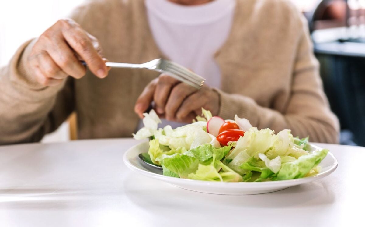 Photo shows someone in a hospital or care setting about to eat a large bowl of salad at a white table