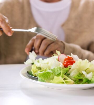 Photo shows someone in a hospital or care setting about to eat a large bowl of salad at a white table