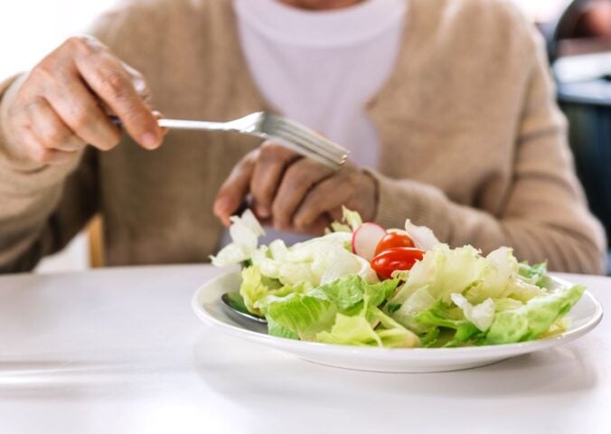 Photo shows someone in a hospital or care setting about to eat a large bowl of salad at a white table