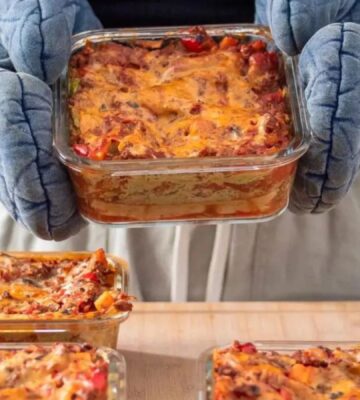 Photo shows someone wearing blue oven gloves and holding up a large dish full of vegan lasagna