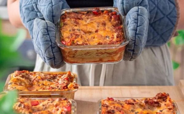 Photo shows someone wearing blue oven gloves and holding up a large dish full of vegan lasagna