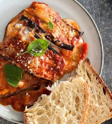 A plate of vegan and dairy-free aubergine parmigiana served alongside white bread and vegan parmesan