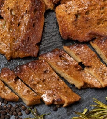 Photo shows several seitan steaks on a slate alongside rock salt, pepper, and rosemary