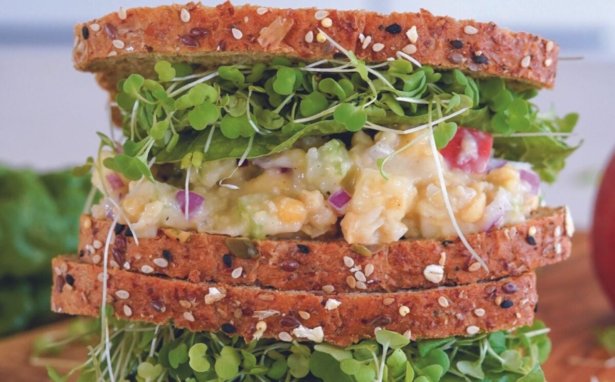 a vegan apple and chickpea salad sandwich with brown bread, lettuce, and sprouts