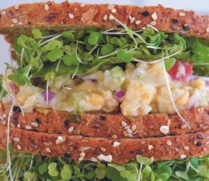 a vegan apple and chickpea salad sandwich with brown bread, lettuce, and sprouts