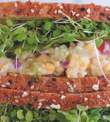 a vegan apple and chickpea salad sandwich with brown bread, lettuce, and sprouts