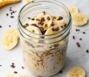 a glass jar full of vegan chocolate banana overnight oats topped with sliced banana and dark chocolate chips