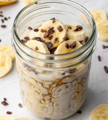 a glass jar full of vegan chocolate banana overnight oats topped with sliced banana and dark chocolate chips