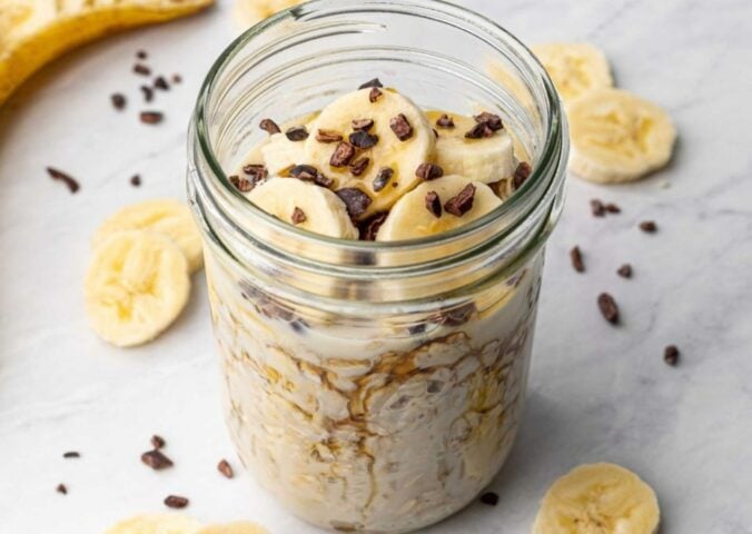 a glass jar full of vegan chocolate banana overnight oats topped with sliced banana and dark chocolate chips