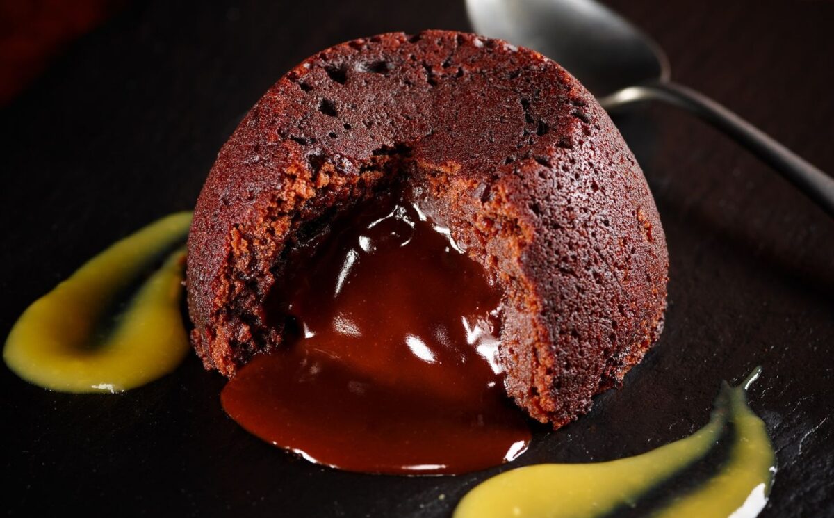a vegan chocolate fondant cake on a plate with mango coulis