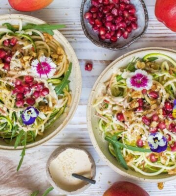 vegan courgetti, tahini, and apple salad garnished with edible flowers and pomegranate