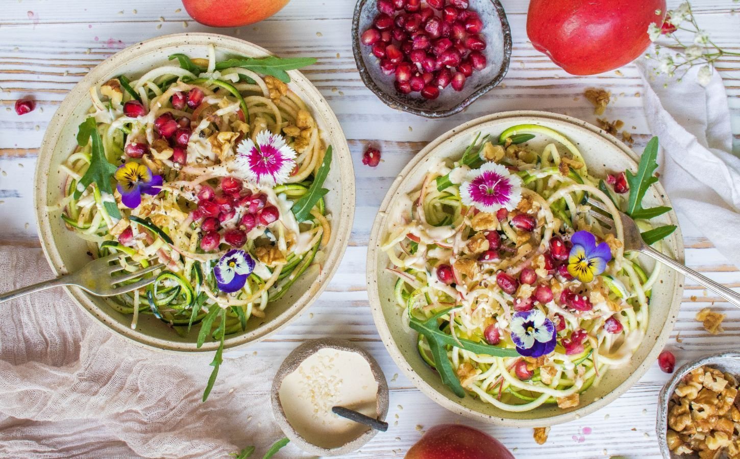vegan courgetti, tahini, and apple salad garnished with edible flowers and pomegranate