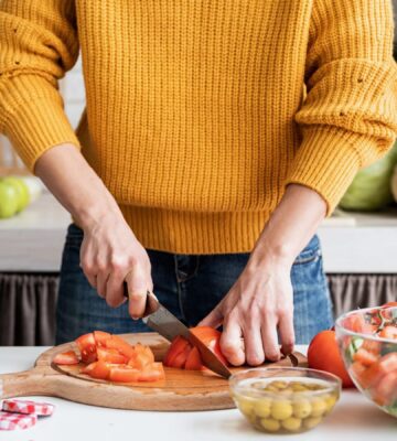 Photo shows someone cutting fresh vegetables on a wooden chopping board in the kitchen