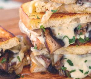 a fried portobello mushroom and spicy vegan cheese sauce sandwich with caramelized onions