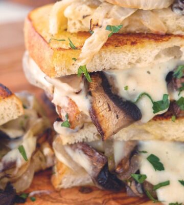 a fried portobello mushroom and spicy vegan cheese sauce sandwich with caramelized onions