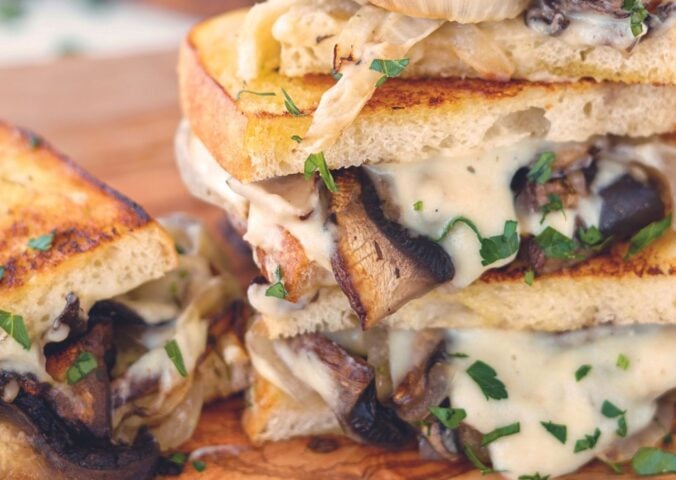 a fried portobello mushroom and spicy vegan cheese sauce sandwich with caramelized onions