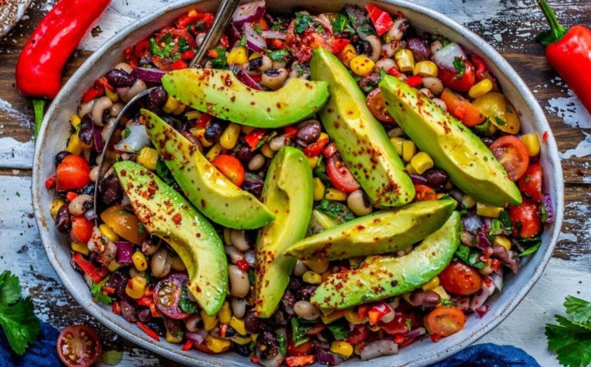 Photo shows a large bowl of Mexican bean salad topped with spices and sliced avocado