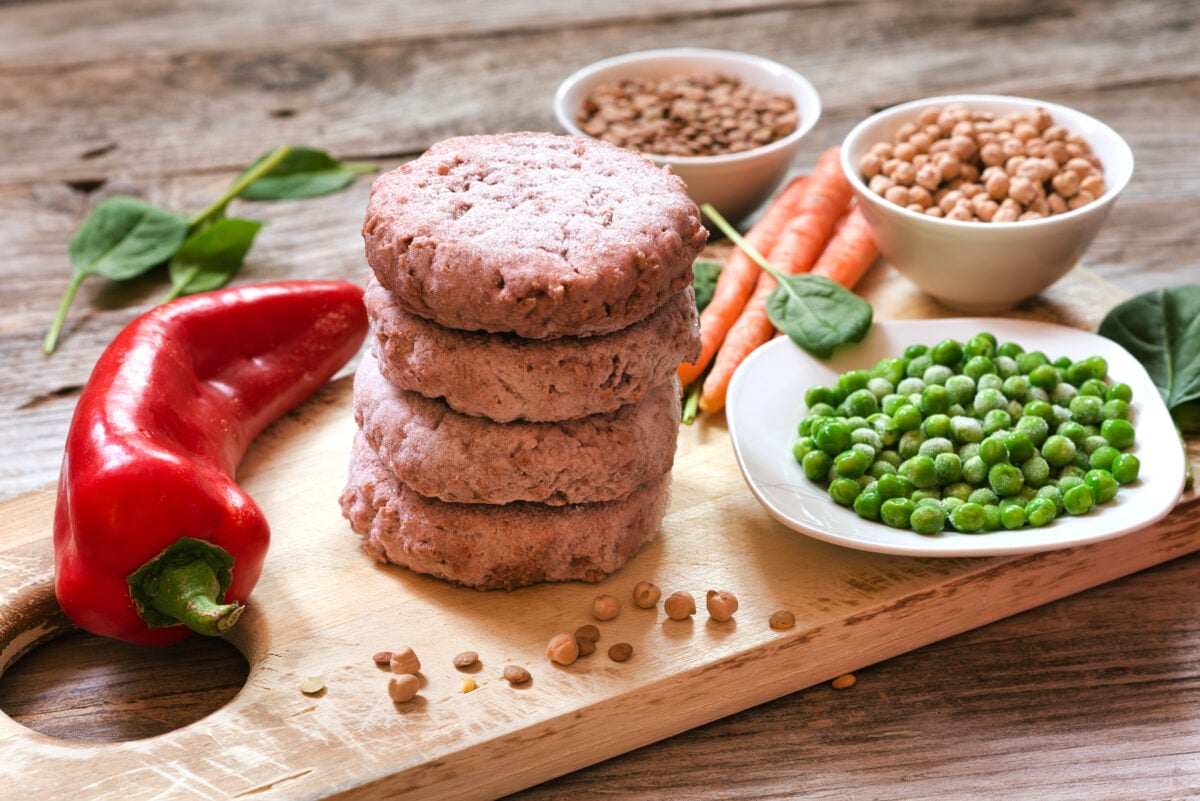 Photo shows dishes of various vegetables on a chopping board with a stack of meat-free burger patties