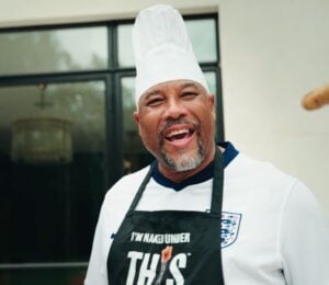 Football player John Barnes wearing an apron from vegan meat brand THIS and holding a plant-based sausage