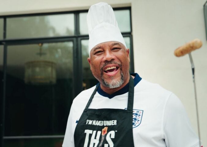 Football player John Barnes wearing an apron from vegan meat brand THIS and holding a plant-based sausage
