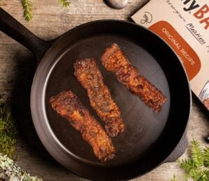 Photo shows the packaging of MyForest Foods Co's plant-based mycelium bacon as well as three slices browned in a cast iron pan