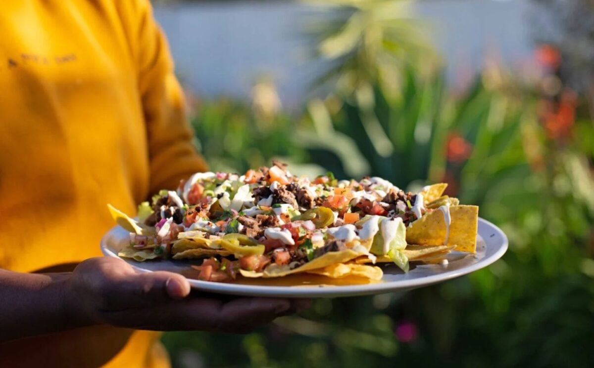 Photo shows someone holding a large plate of loaded vegan nachos
