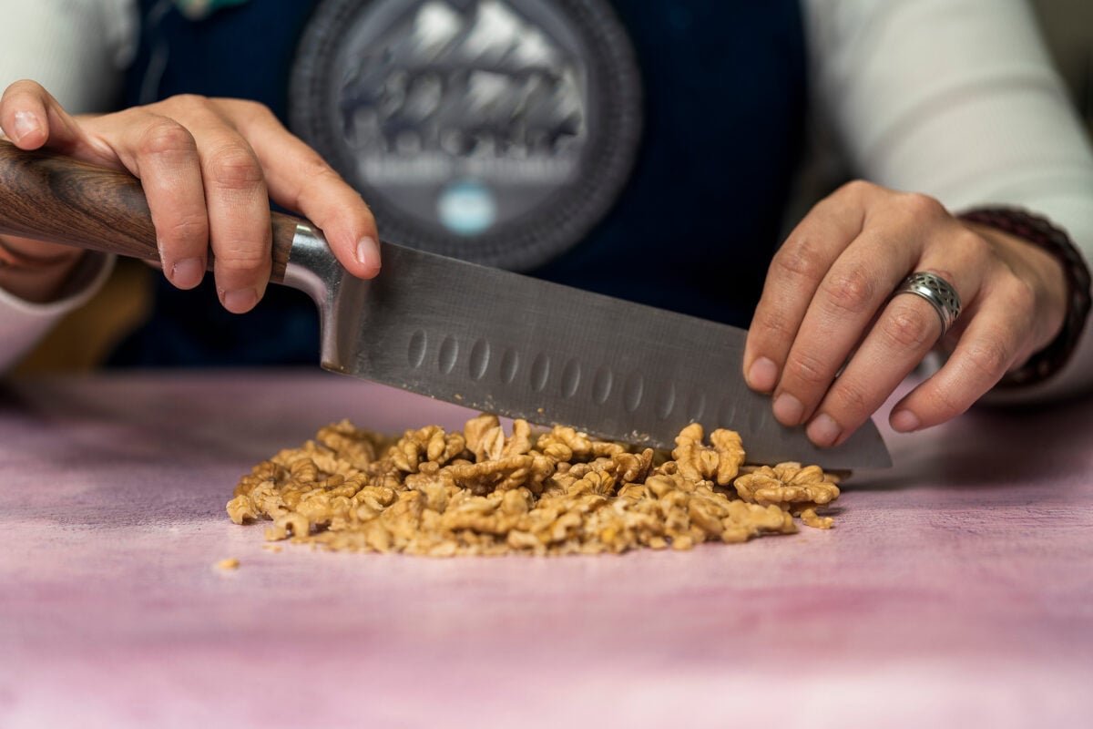Photo shows someone's hands as they chop up a large pile of walnuts