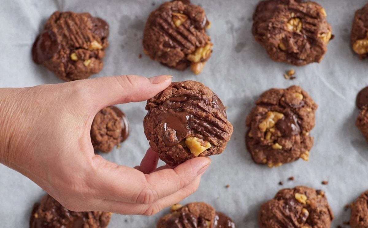 Photo shows a hand holding up a single chocolate walnut cookie above a tray of the same