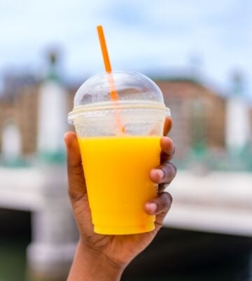 Photo shows someone holding up a plastic cup with a straw full of orange juice