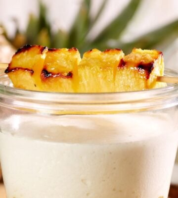 vegan pineapple, coconut, and chocolate crumble layered in a glass and topped with a grilled skewer of pineapple