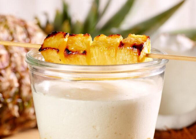 vegan pineapple, coconut, and chocolate crumble layered in a glass and topped with a grilled skewer of pineapple