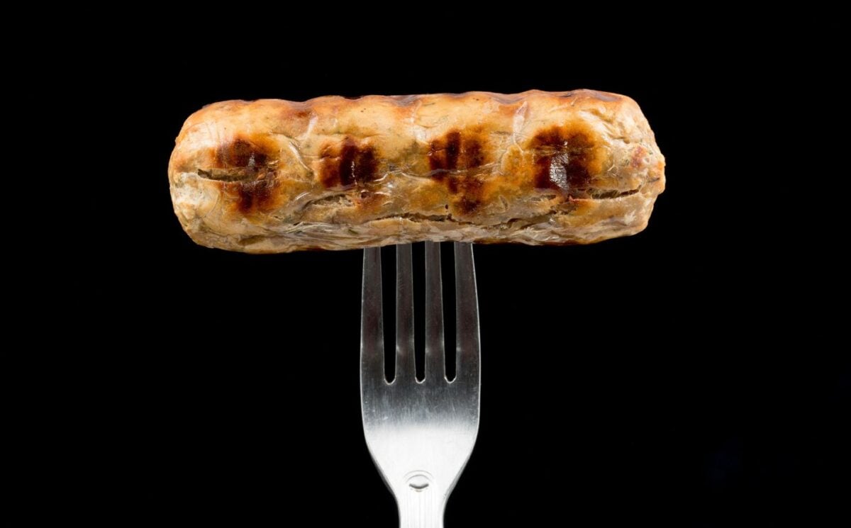 A Quorn sausage on a fork in front of a black background