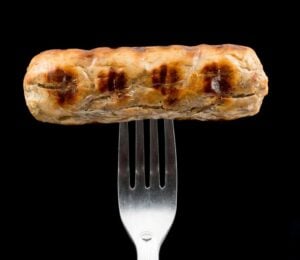 A Quorn sausage on a fork in front of a black background