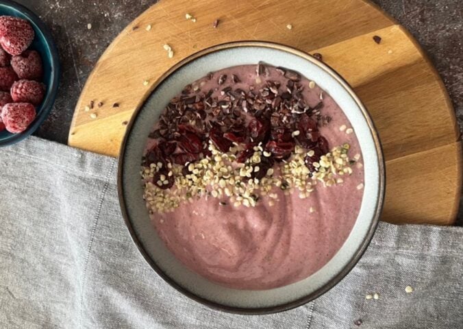 A picture of a vegan raspberry smoothie bowl topped with hemp hearts and cocoa nibs