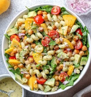 a peach and arugula pasta salad with tomato, peach, and other plant-based ingredients