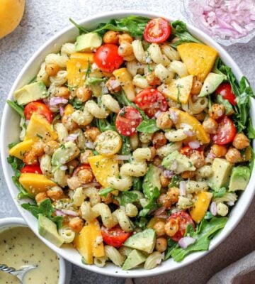 a peach and arugula pasta salad with tomato, peach, and other plant-based ingredients