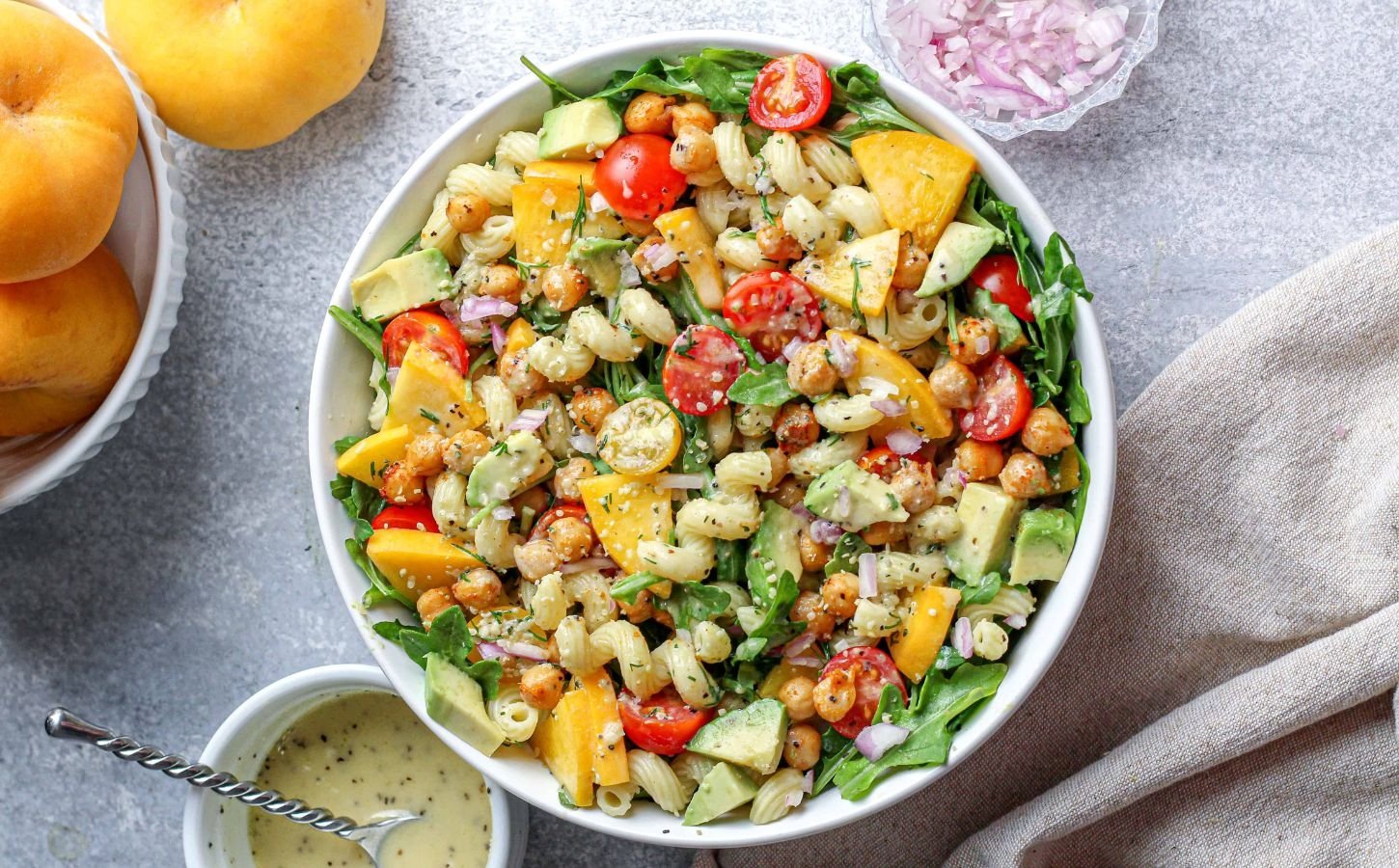 a peach and arugula pasta salad with tomato, peach, and other plant-based ingredients