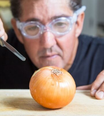 Photo shows a man in swmming goggles about to cut into a white onion with a scalpel